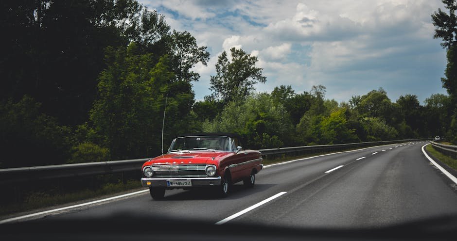Vintage red convertible cruising along a scenic highway with lush greenery.