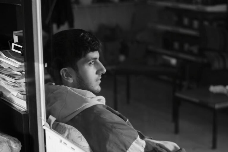A thoughtful young man gazes into the distance in a monochromatic indoor setting.