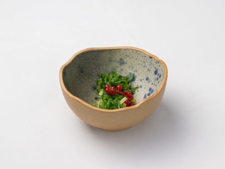 Close-up of a fresh green seaweed salad with red berries in a ceramic artisan bowl.