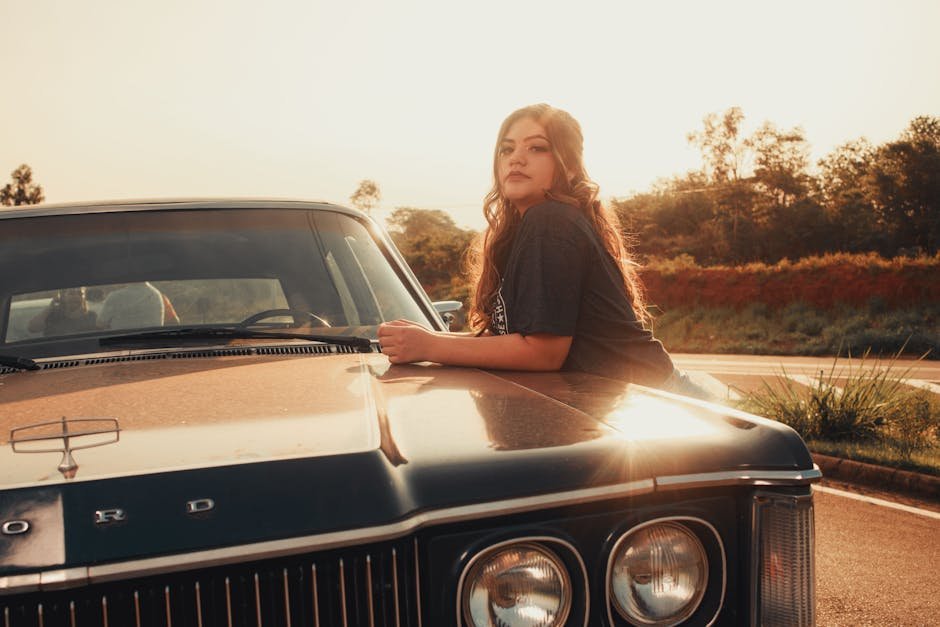A woman poses on a vintage Ford car at sunset, showcasing style and classic automotive design.