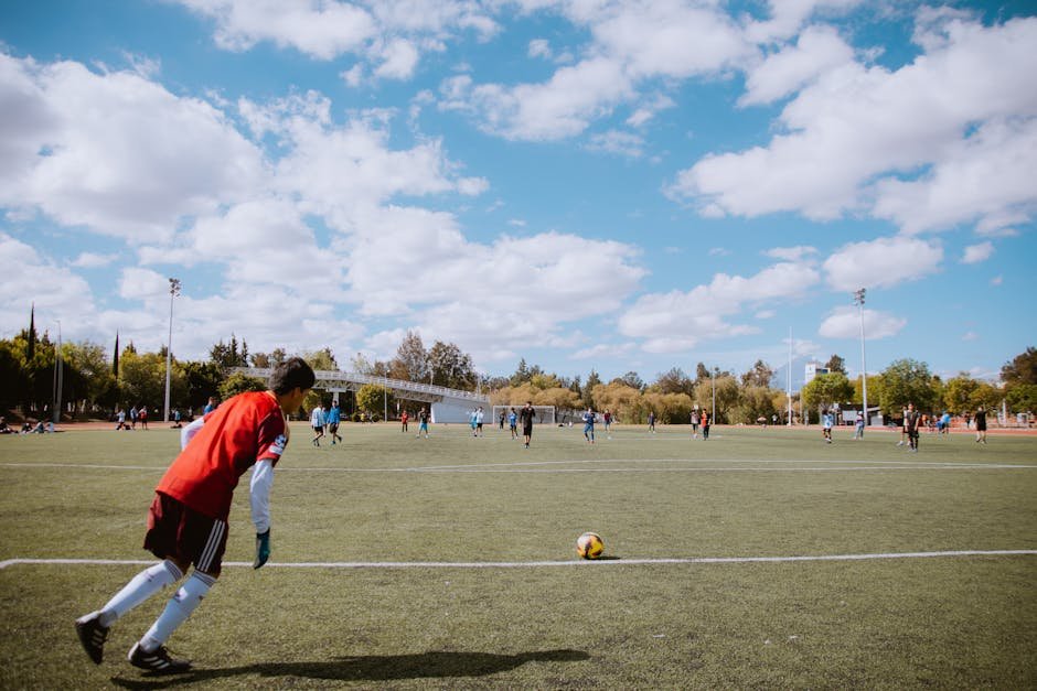 Soccer players on a field under a bright blue sky, competing in a friendly match.