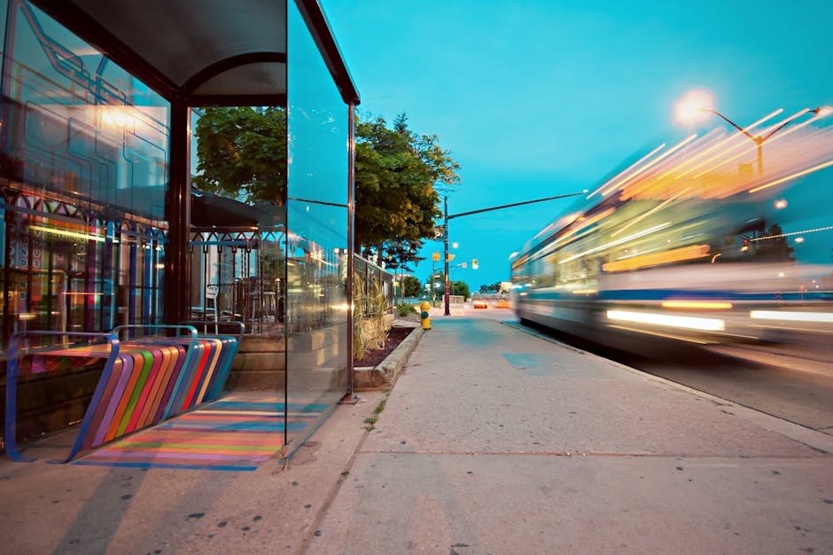 Colorful city bus stop with vibrant benches, blurred motion of a passing bus at dusk.