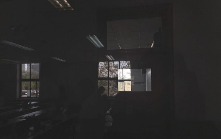 Dark classroom with reflections on glass highlighting trees and windows, creating a moody ambiance.