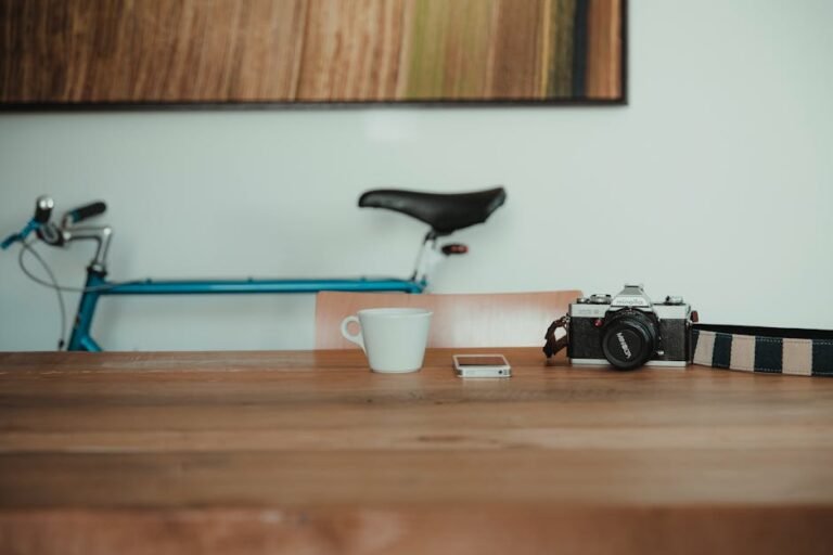 A vintage camera alongside a sleek bicycle, a coffee cup, and a cellphone on a wooden table, blending old and new styles.
