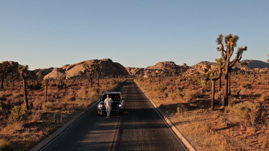 Desert road in Joshua Tree with car and lone traveler at sunset.